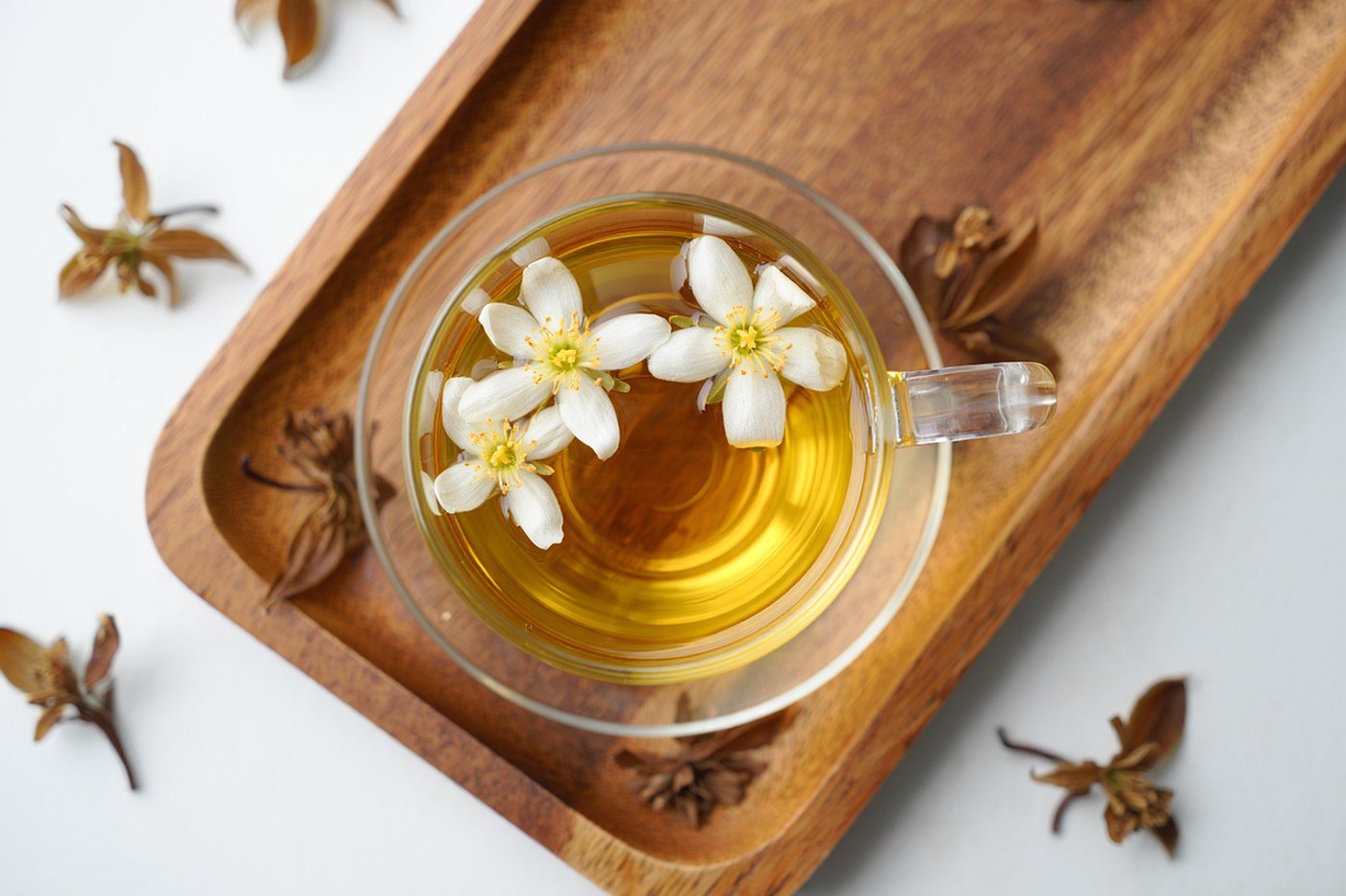 Tasse en verre d'infusion aux plantes avec herbes séchées et pétales sur une soucoupe en bois