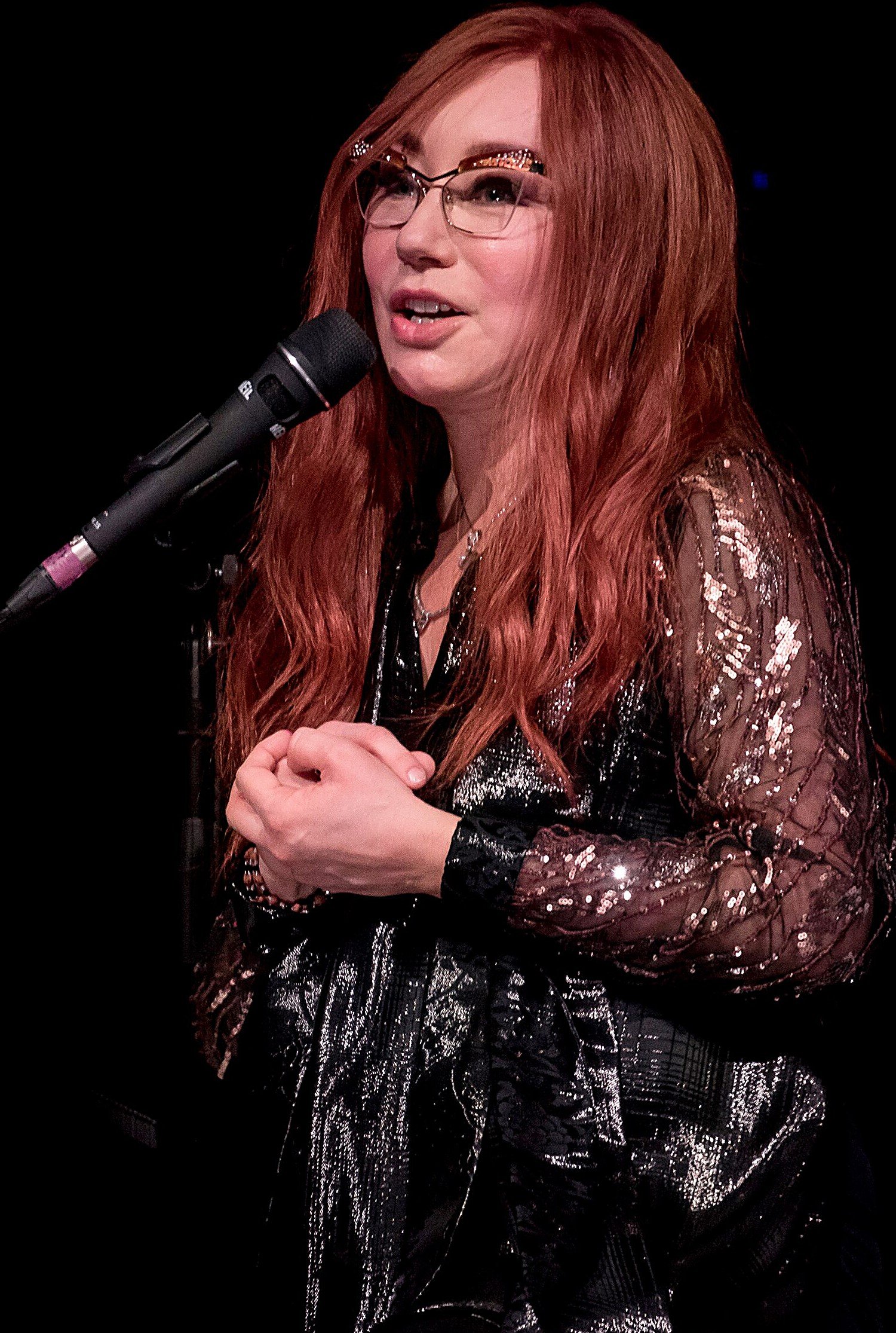 Tori Amos en concert, chevelure rousse et lunettes, chantant au micro