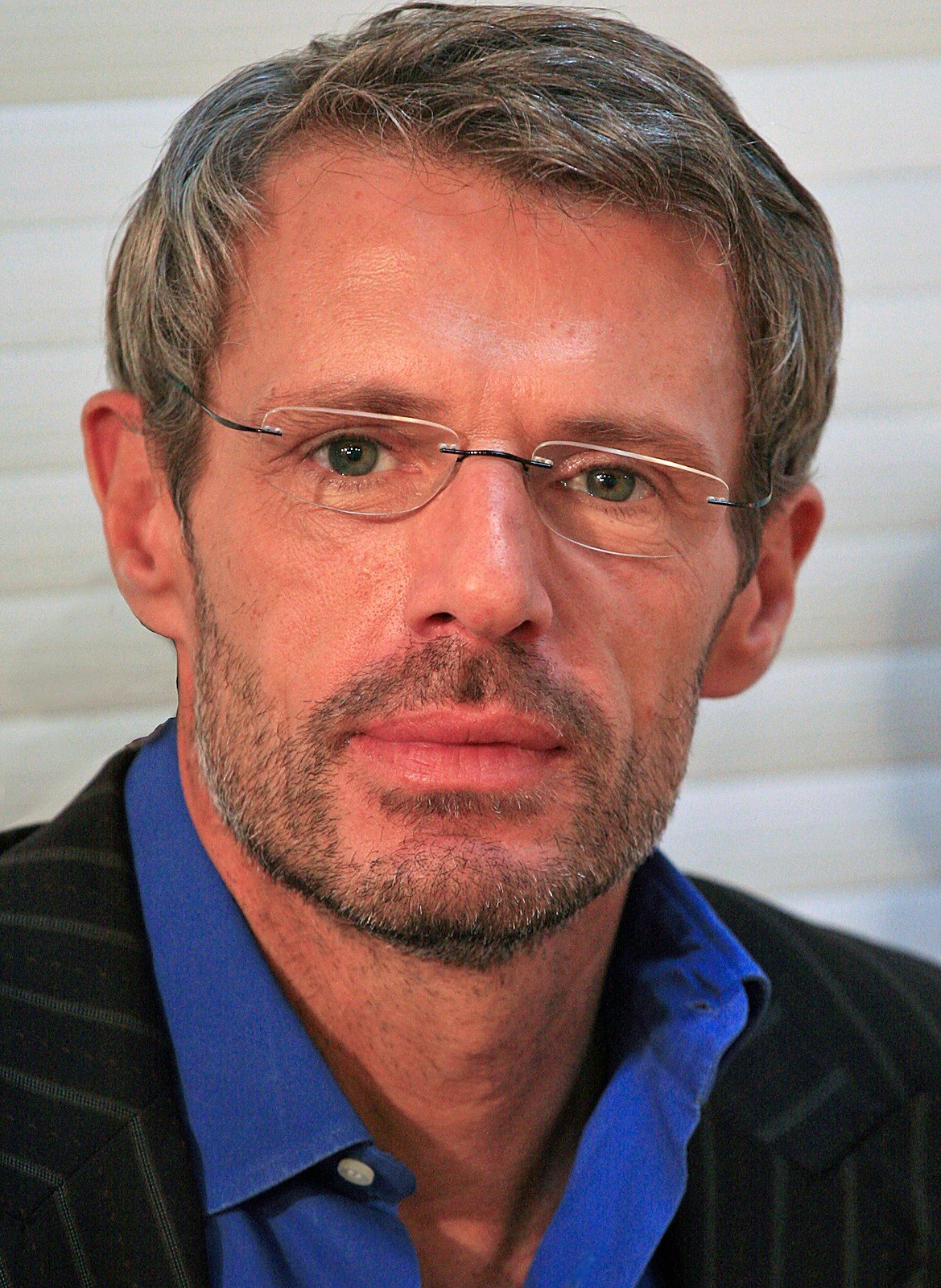 Portrait de Lambert Wilson, lunettes fines et chemise bleue