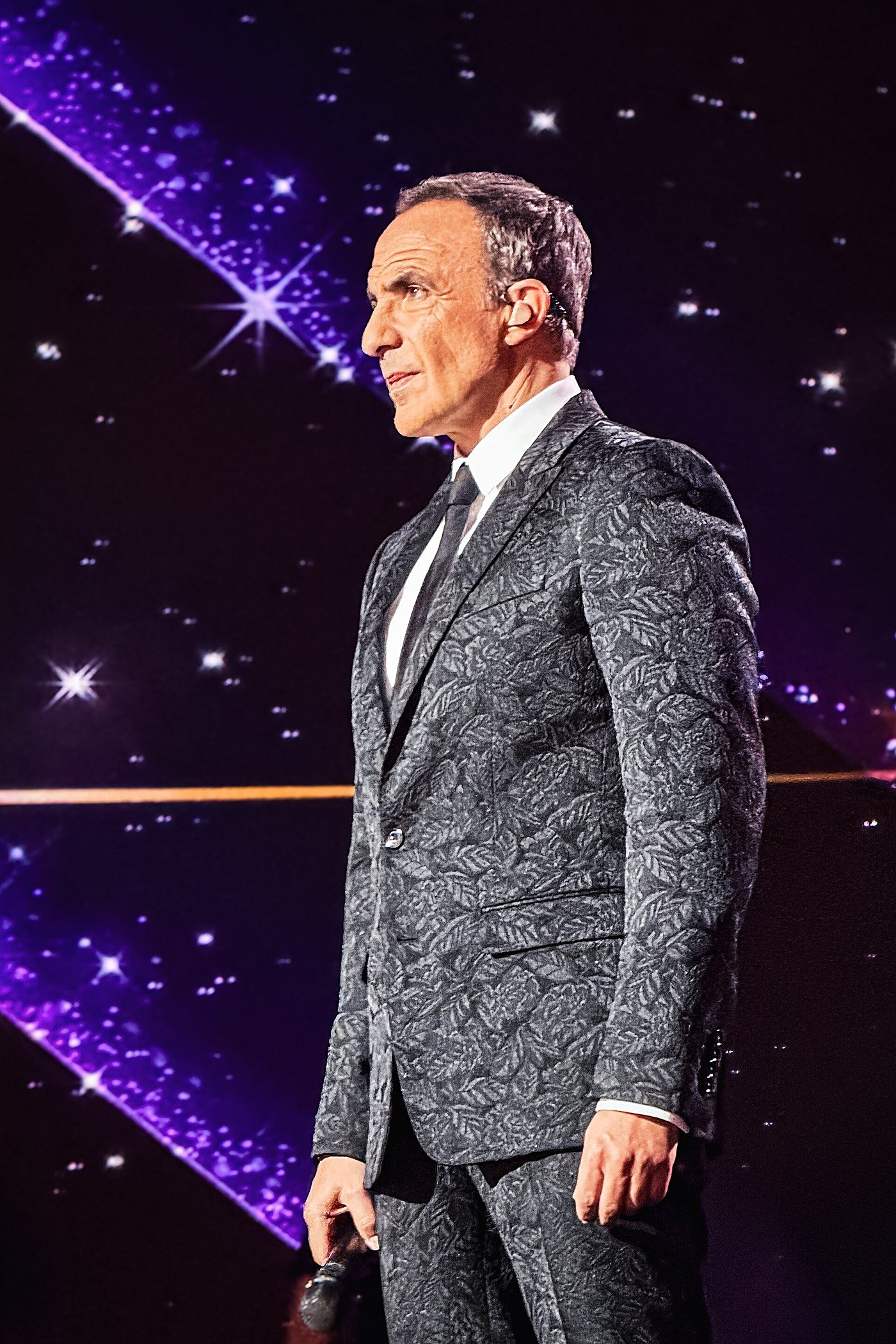 Nikos Aliagas sur la scène, en costume, micro à la main