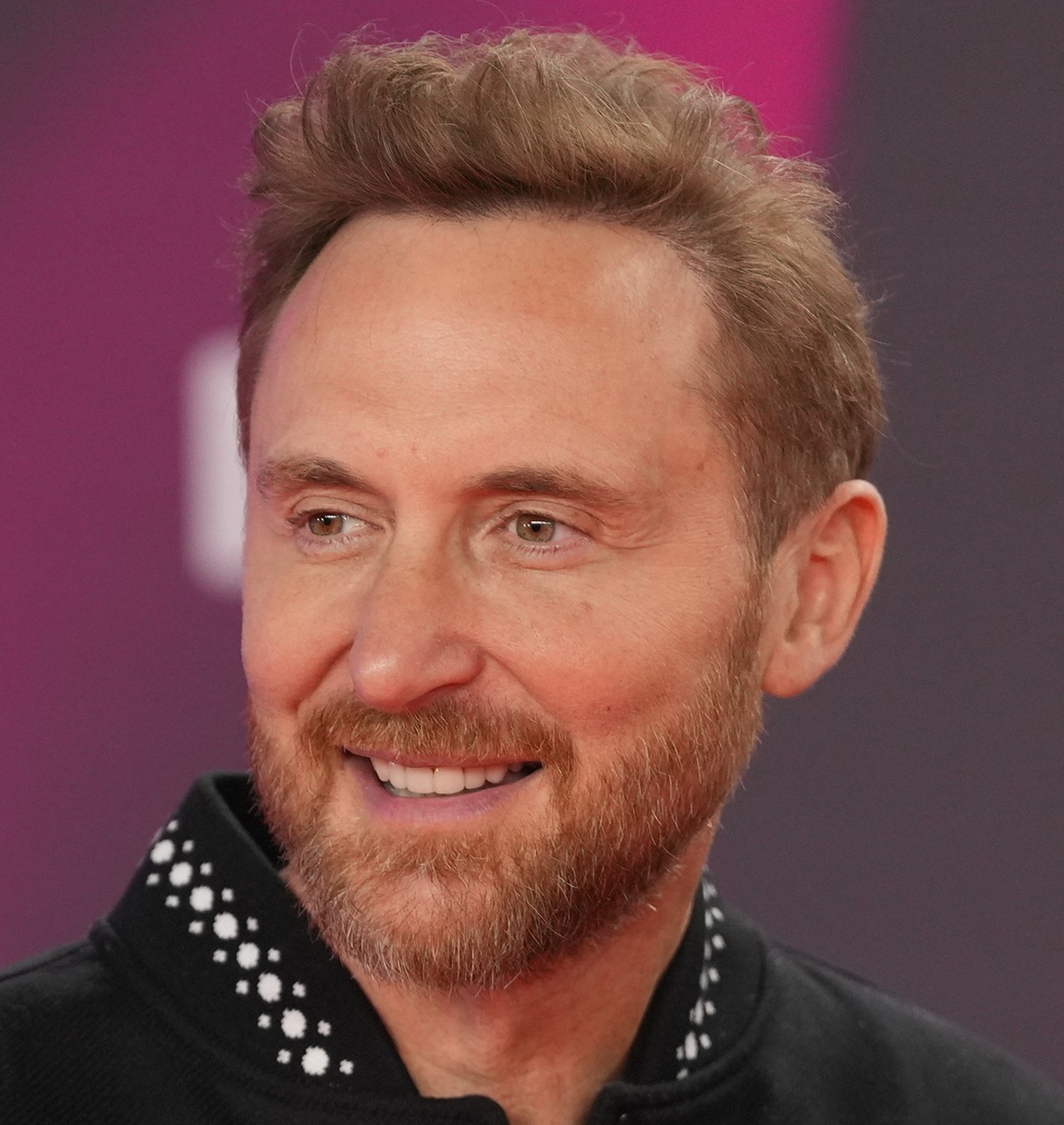 Le DJ et producteur français David Guetta, portrait souriant sur fond magenta